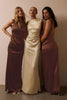 Three women modeling floor-length satin bridesmaid dresses in a studio setting. The center model wears a champagne gold dress, while the two side models wear matching dusty rose-brown dresses.