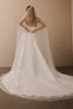 A woman wearing a strapless white wedding gown and a long sheer veil, photographed from behind against a plain beige wall and floor.