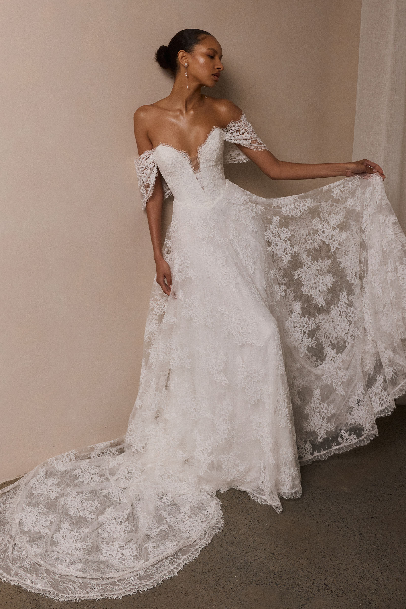 A woman wearing a white off-the-shoulder lace wedding gown with a deep V neckline and a full layered skirt_XS_
