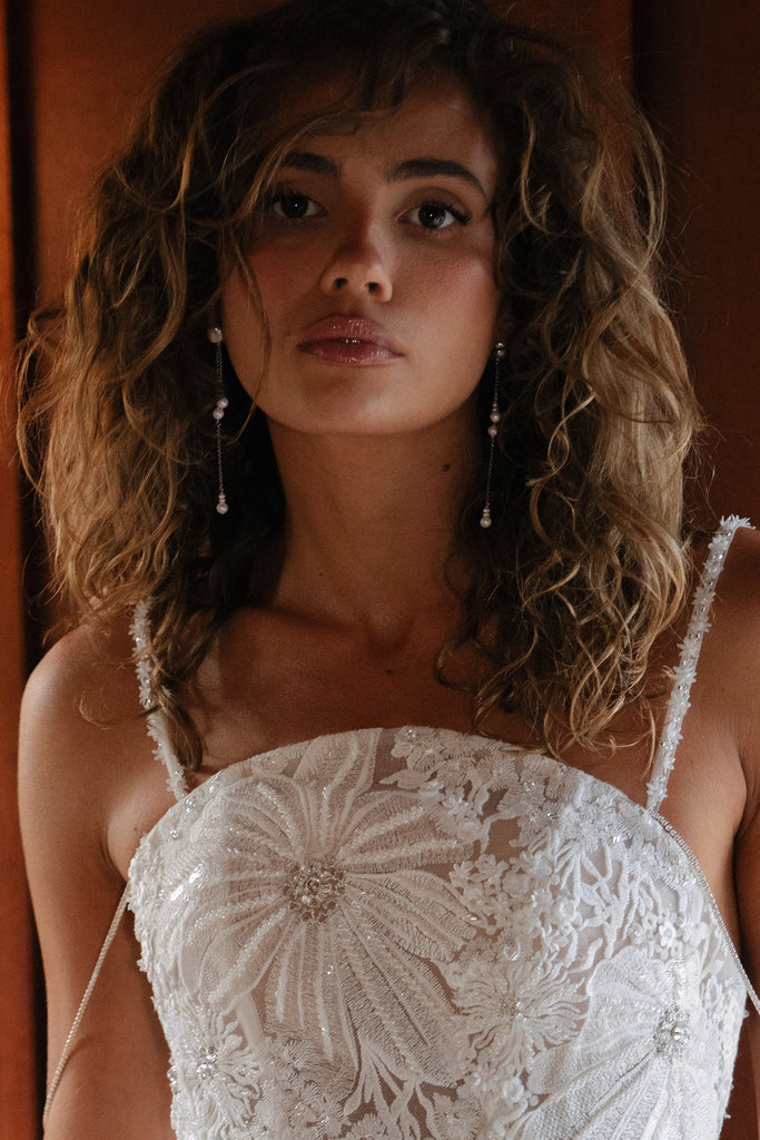 Woman wearing a white lace dress with long pearl earrings