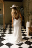 Woman in a wedding dress with a backless feature and a white hat standing on a black and white checkered floor.