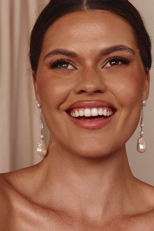 Woman wearing pearl earrings with a neutral background