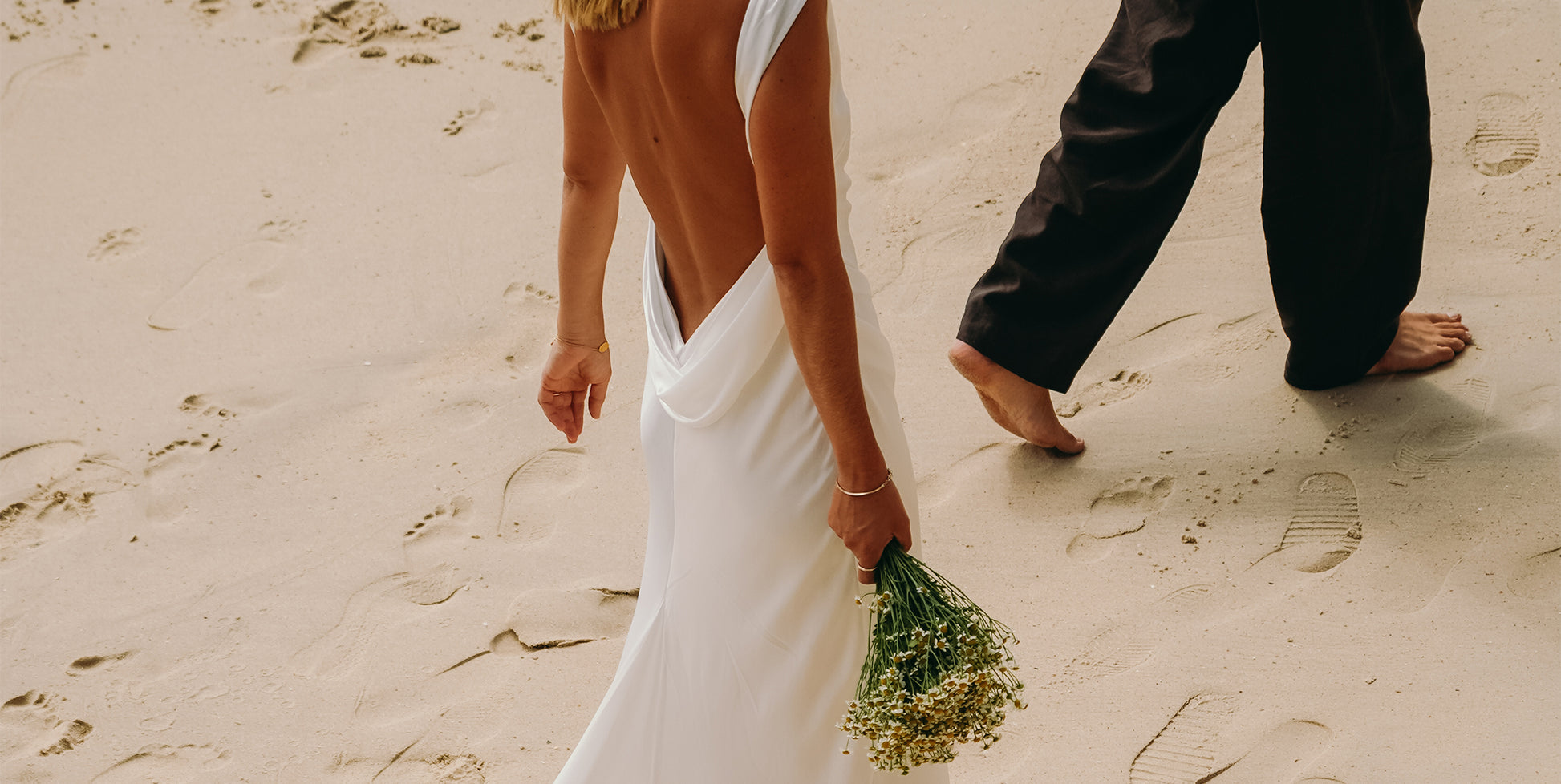 A bride and groom walking on the beach in wedding attire.