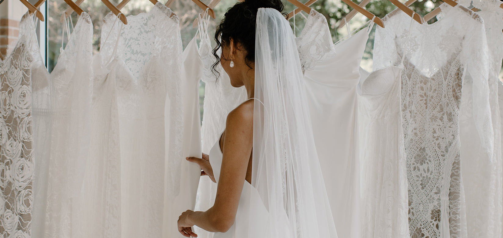 bride looking at wedding dresses hung on rack