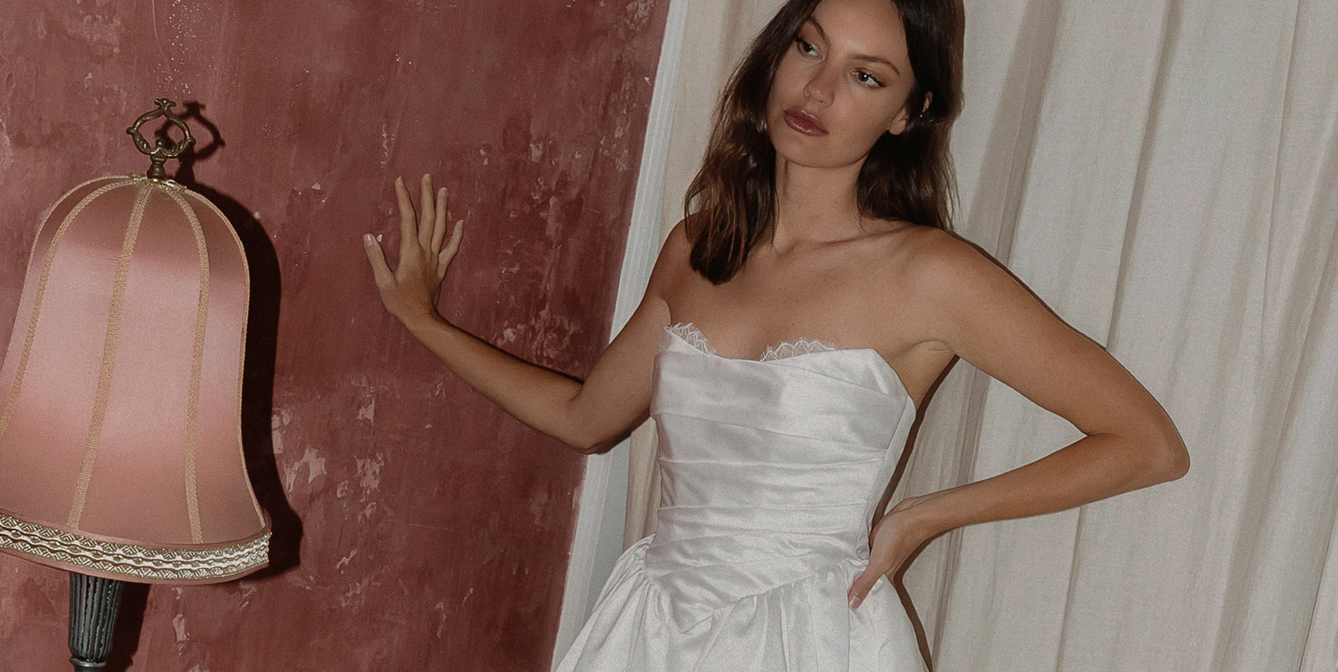 Woman in a strapless wedding dress standing against a textured wall.